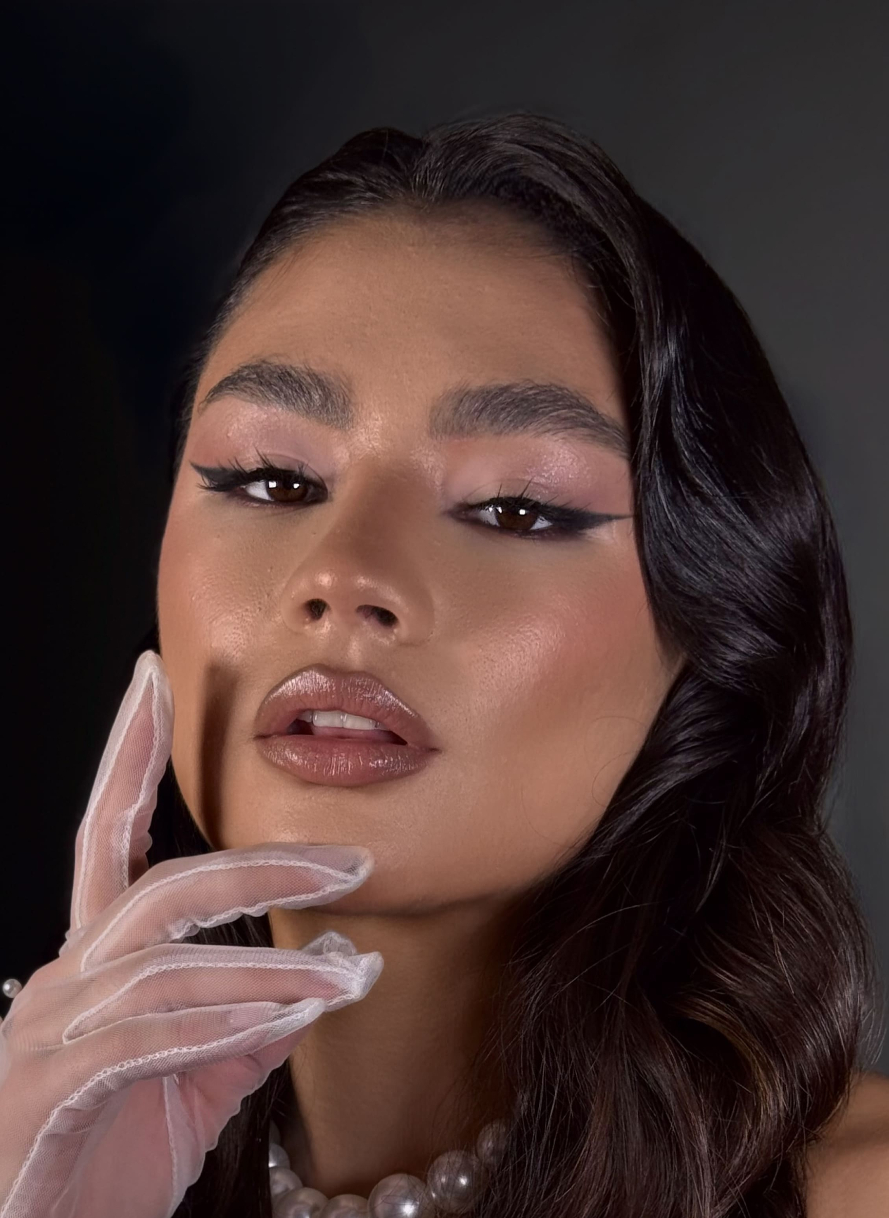 Mujer con cabello rojo intenso, labios brillantes y guantes largos rojos posando con mirada lateral.