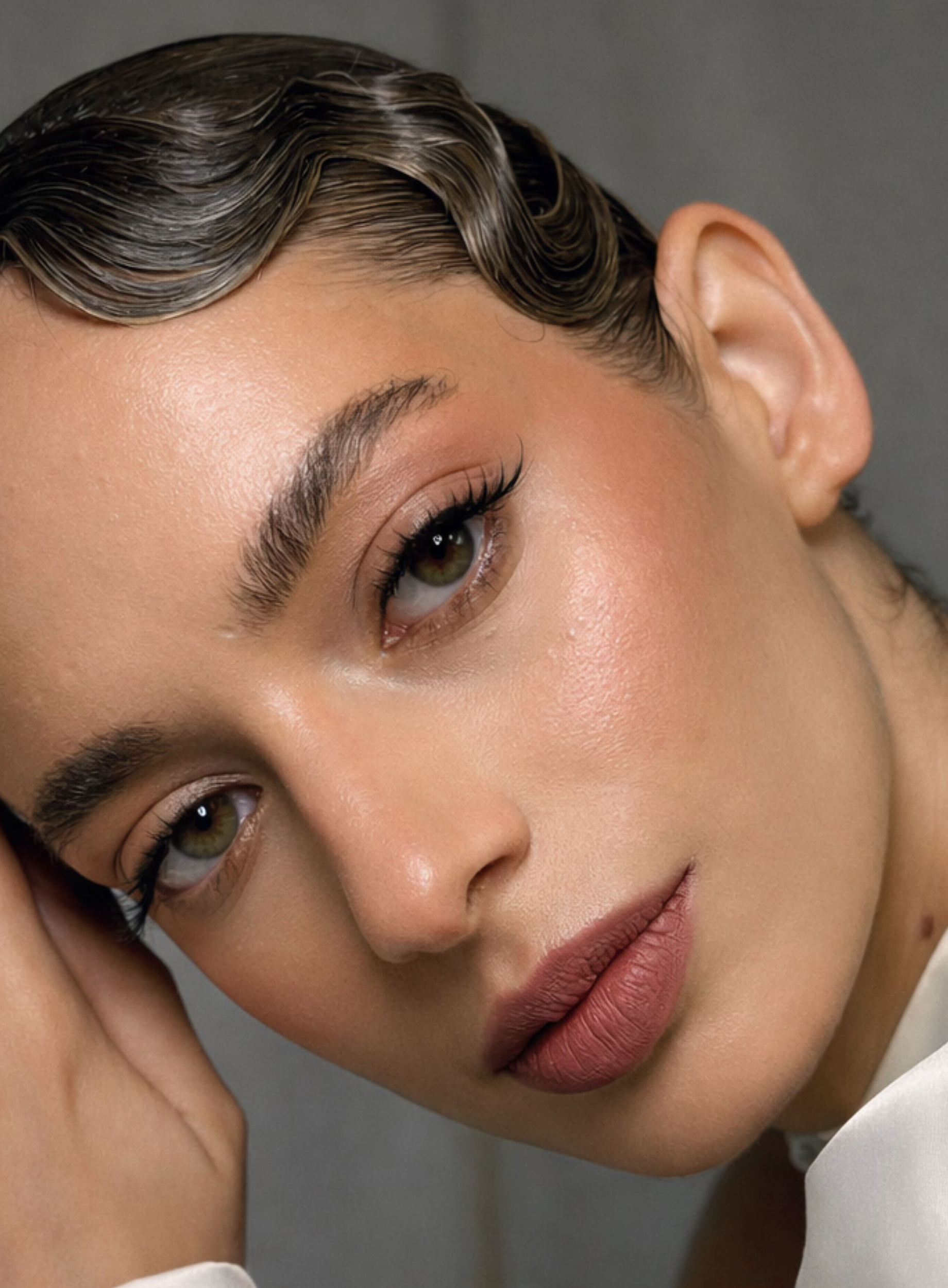 Primer plano de una mujer con piel tersa y maquillaje natural, labios mate y cejas definidas.